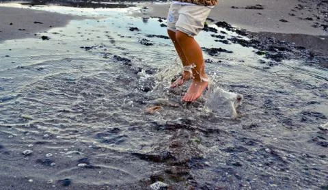 Autumn seashore. A child girl jumps barefoot through the sea puddles. Childre Stock Photos