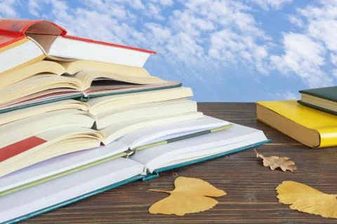 Autumn. Stack of open books and yellow leaves  on the table against blue sky Stock Photos