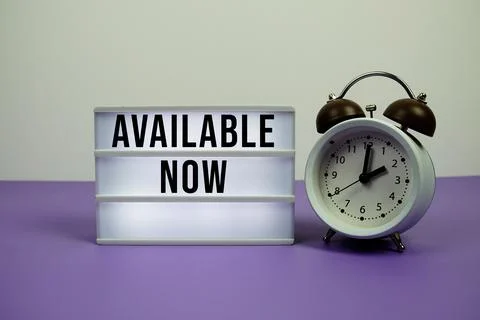 Available Now text on LED lightbox with alarm clock on purple background Stockfoto's