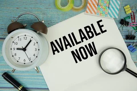 Available Now text written on notepad with alarm clock and magnifying glass.. Stock Photos