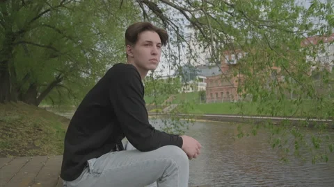 The average plan. In summer, the guy sits on a wooden pier near the water, looks Stock Footage 136652831