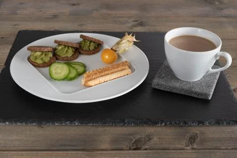 Avocado on bread on a white plate with a cup of coffee. Stock Photos