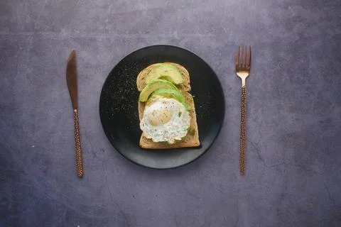 Avocado, brown bread, egg and rosemary on black background 스톡 사진