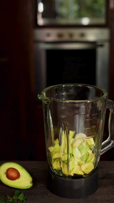 Avocado chunks inside blender jar on wooden kitchen counter Video stock 331773312