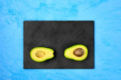 Avocado cut in half, one slice with core on a gray slate are arranged on a li Stock Photos