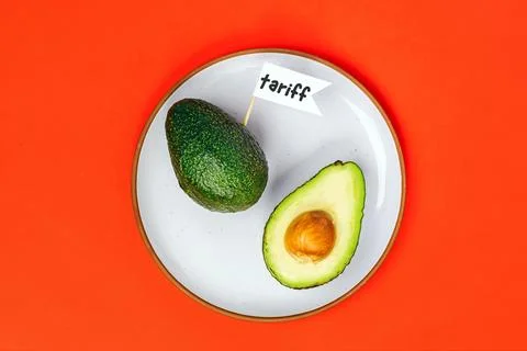 Avocado cut open on a plate with a small flag that reads tariff Stock Photos
