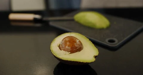 An avocado on a modern black table in the kitchen. Slow motion. Video stock 148554899