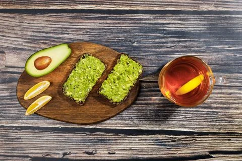 Avocado paste is spread on whole wheat bread. Near slices of lemon and half a Stock Photos