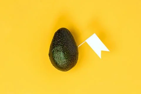 Avocado with a small white flag on a vibrant yellow background Stock Photos
