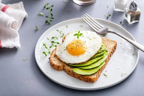 Avocado toast on a toasted multigrain bread with a fried egg Stock Photos