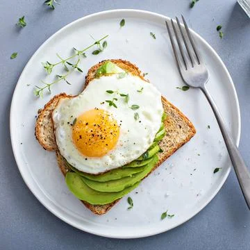 Avocado toast on a toasted multigrain bread with a fried egg Stock Photos