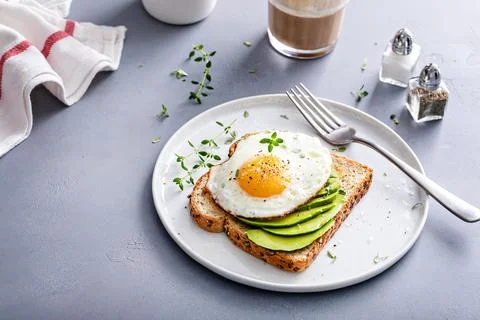 Avocado toast on a toasted multigrain bread with a fried egg Stock Photos