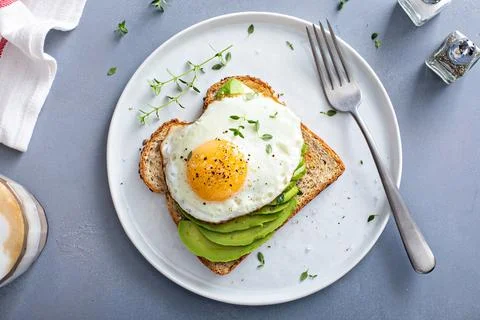 Avocado toast on a toasted multigrain bread with a fried egg Stock Photos