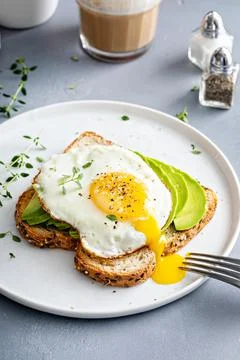 Avocado toast on a toasted multigrain bread with a fried egg Stock Photos