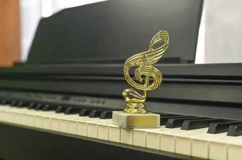Award statue in shape of treble clef on sleek piano, representing achieveme.. Stock Photos