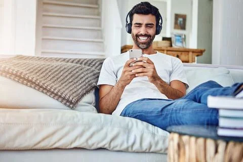 Awesome songs for solo time. a man relaxing on the sofa while using his phone Stock Photos