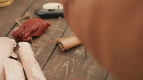 Awl piercing cone shaped leather sheath on weathered wooden workbench with tied Vidéo 343683673