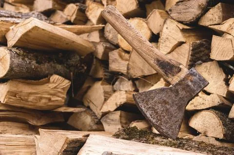 The ax is stuck in a log against the backdrop of chopped firewood lying in a Stock Photos