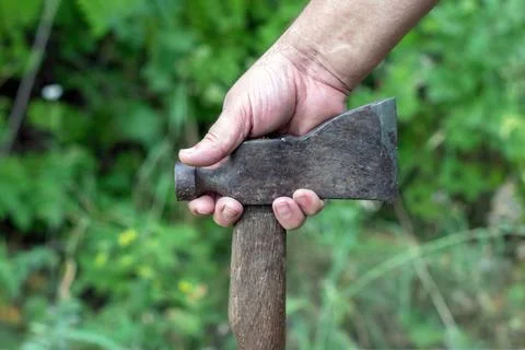 An axe in a man's hand. Against the background of an overgrown garden. Stock Photos