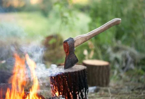 Axe in tree stump and campfire with smoke Stock Photos