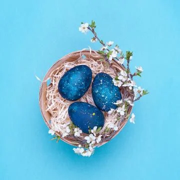 Azure easter eggs in a basket with flowers on a violet background. Square pho Stock Photos