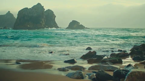 Azure sea waves roll over sandy coast with stones in shallow water 库存影片 329695776