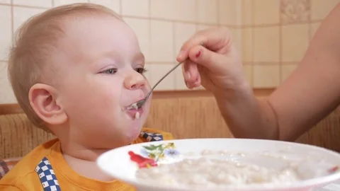 Baby 2 years old eats porridge with a spoon. Mom sits next to the boy. home Stock Footage 74714038