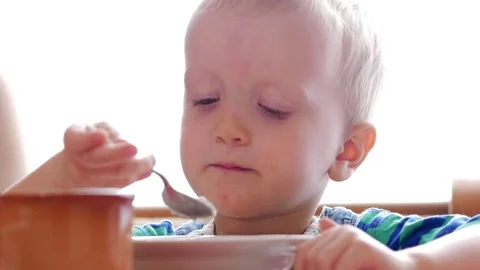 Baby 2 years old eats porridge with a spoon. Mom sits next to the boy. home Stock Footage 74714930