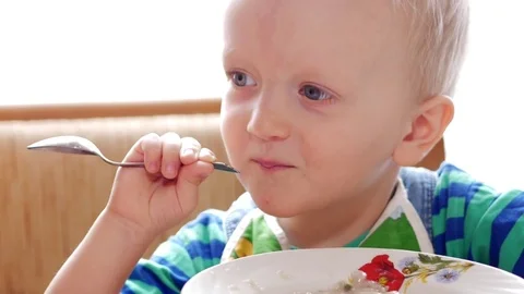 Baby 2 years old eats porridge with a spoon. Mom sits next to the boy. home Stock Footage 74715779