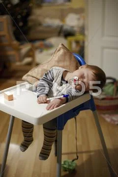 Baby, 8 months, sleeping with pacifier in mouth and a pen in the hand in a ch Stock Photos