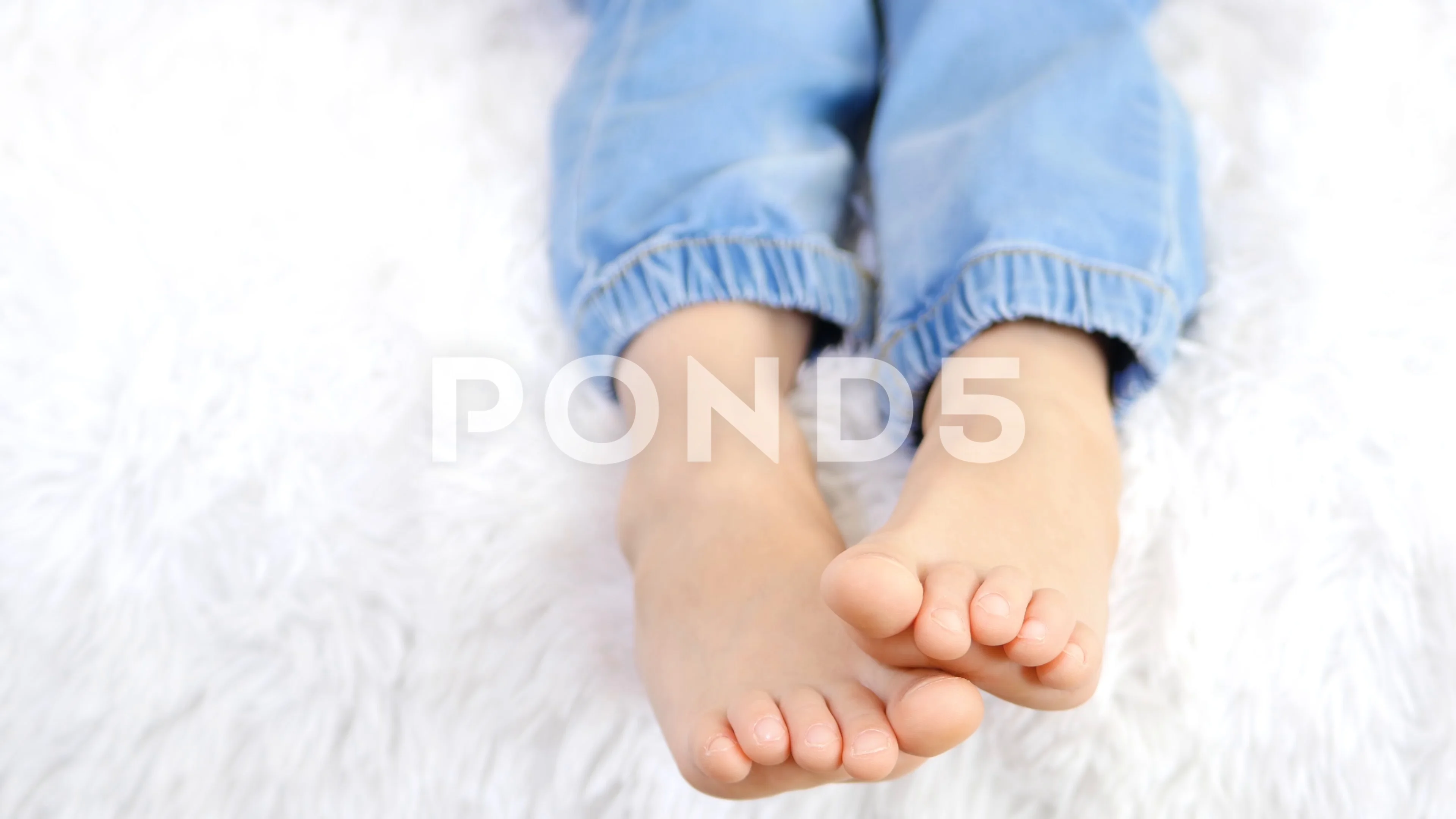 Child with bare feet in jeans. Lying on the bed. Foot barefoot Stock Photo