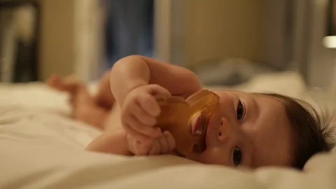 Baby on Bed Looking at Camera and Chewing on Teething Toy Stock Footage 91300698