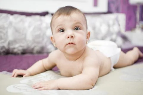 Baby on bed, serious expression. Stock Photos