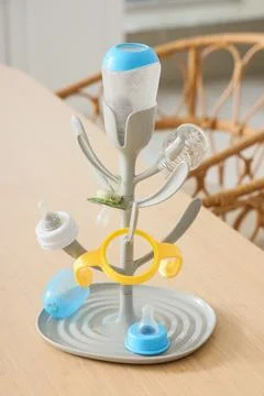 Baby bottle drying rack with pacifiers and teethers on wooden table, nursery  Stock Photos