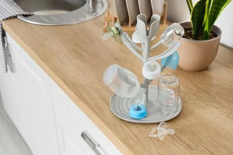 Baby bottles and pacifiers drying on rack in kitchen Stock Photos