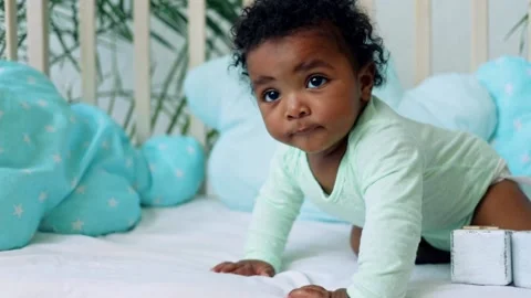 Baby boy African American sits on the bed on a blue cotton bed and wants to Stock Footage
