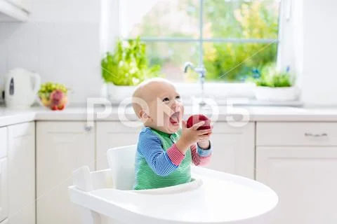 Baby boy eating apple in white kitchen at home Stock Photos