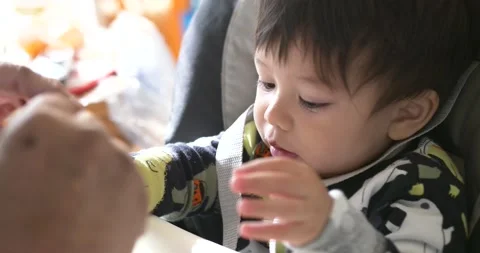 Baby boy holding an orange while being fed Stock Footage 226080649