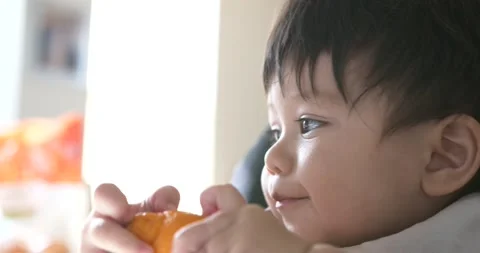 Baby boy holding an orange while being fed Stock Footage 226080734