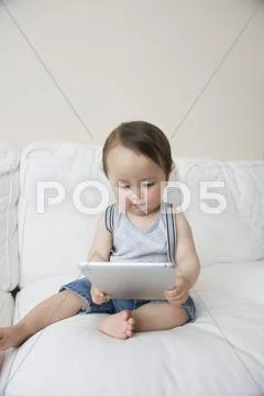 Baby Boy Sitting On Sofa Looking At Digital Tablet