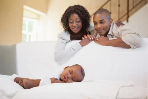 Baby boy sleeping peacefully on couch watched by parents Stock Photos