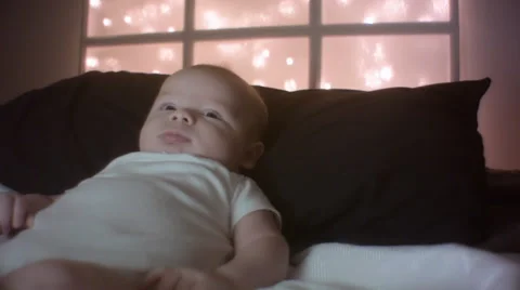 Baby boy smiles and plays with twinkle lights in the background Stock Footage 68749953