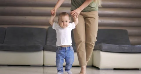 Baby boy taking first steps with mother help at home Stock Footage 145414699