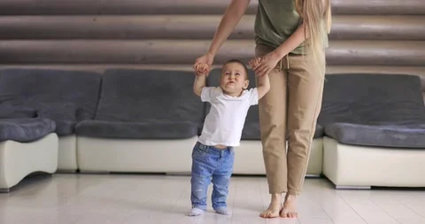 Baby boy taking first steps with mother help at home Stock Footage 145986477