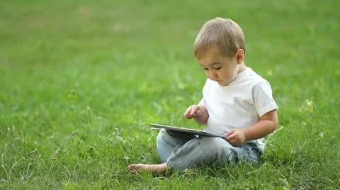 Baby boy working with the Tablet PC sitting on the grass Video stock 11408138