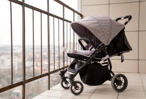A baby carriage with a sleeping child stands on the balcony of a multi-storey Stock Photos