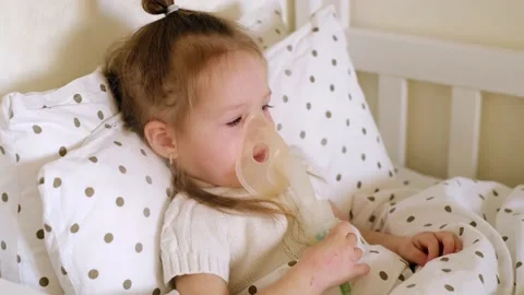 Baby coughs violently while lying in bed with an inhalation mask Stock Footage 165132172