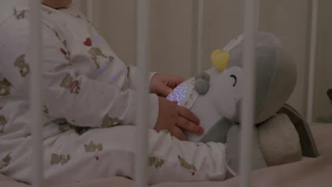 Baby in cozy crib interacts with plush penguin toy, showcasing playful Stock Footage 323233346