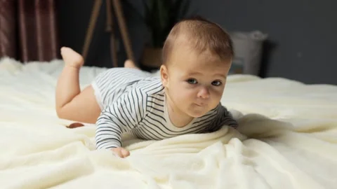 A baby is crawling on a soft, light-colored blanket, showing curiosity and Vídeos de archivo 295676314