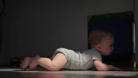 A baby crawls on a tiled floor in low light Stock Footage 322200192